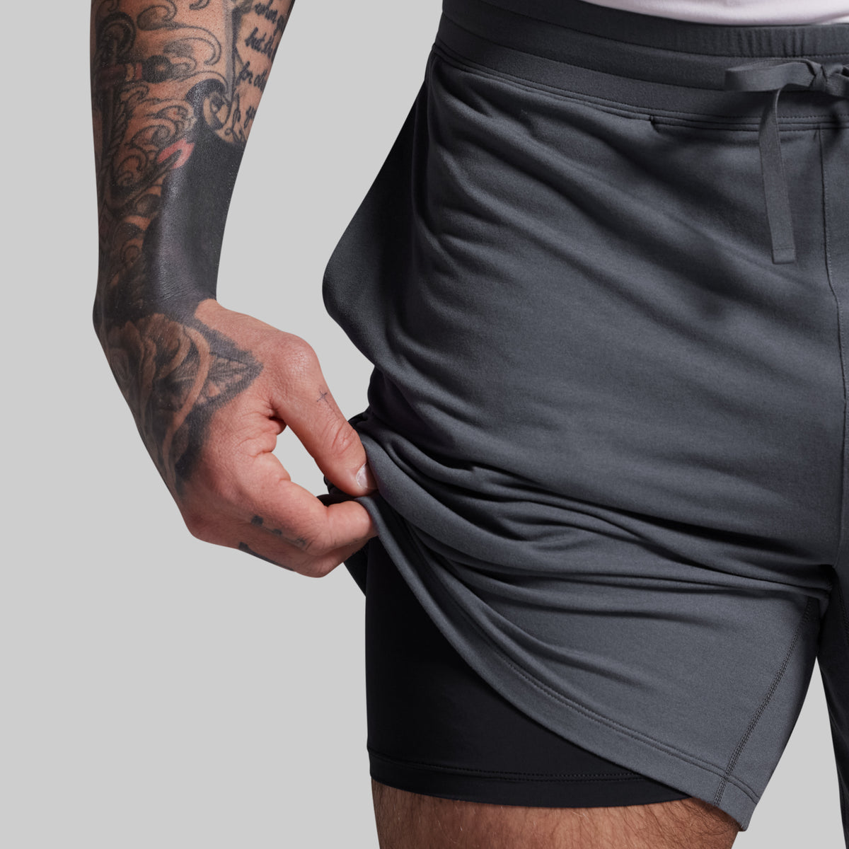 Person wearing gray athletic shorts with a tattooed arm on a light gray background