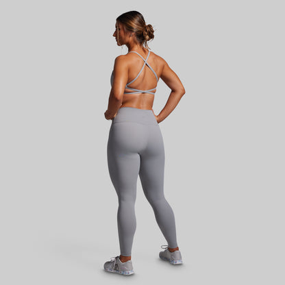 Woman wearing a gray sports bra and leggings on a light gray background