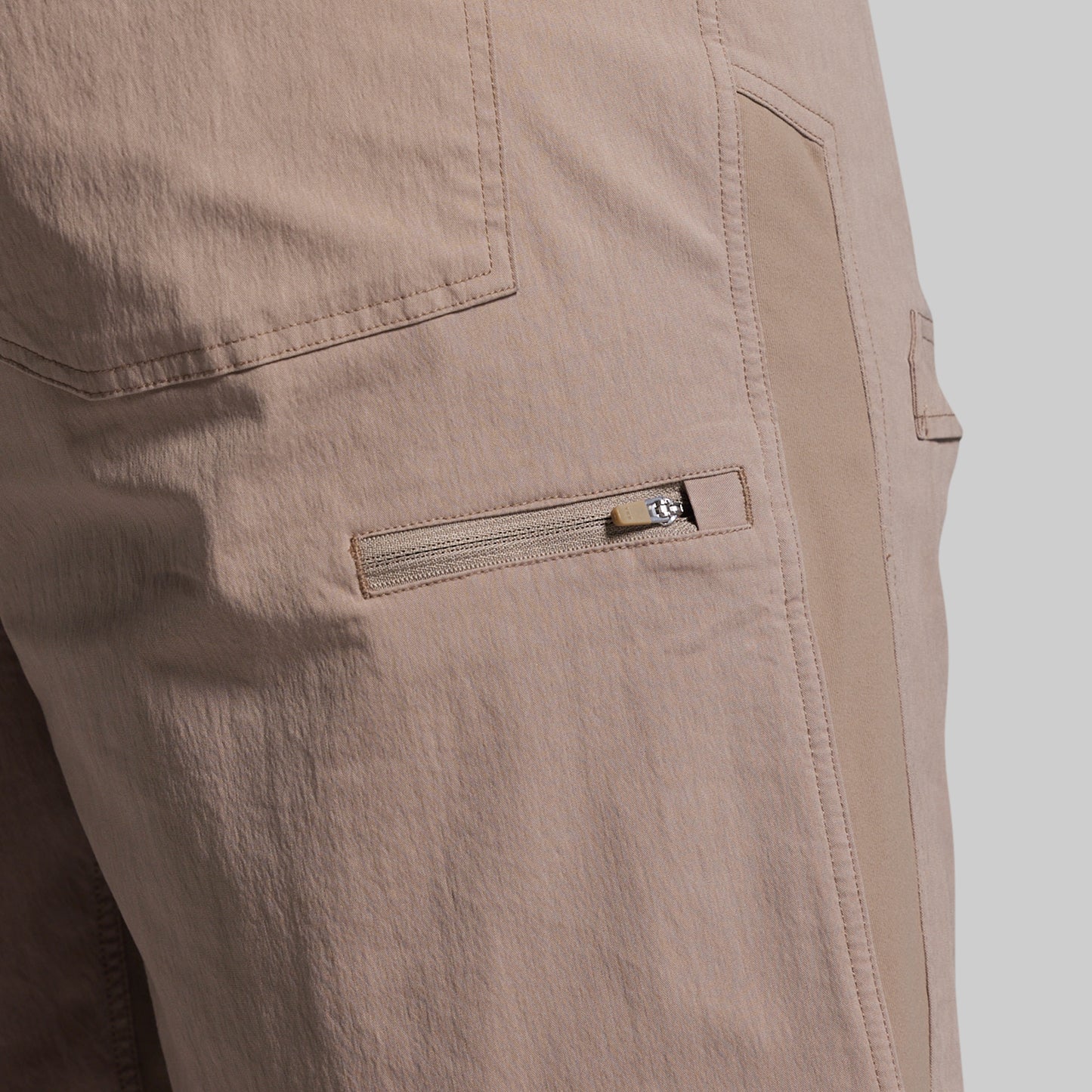 Close-up of beige shorts with a zipper pocket on a light gray background