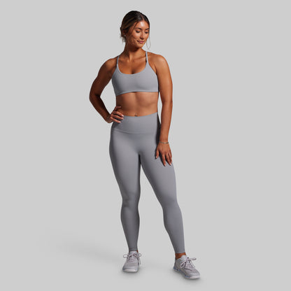 Woman wearing a gray sports bra and leggings set on a light gray background