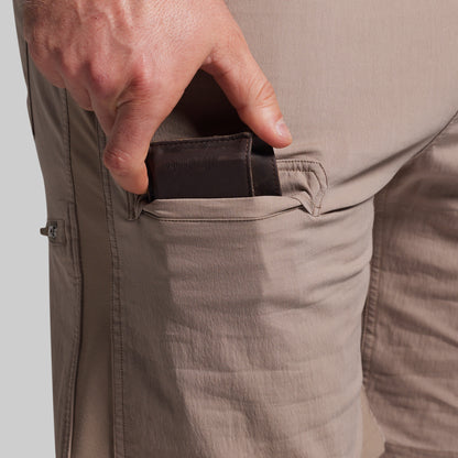 Person wearing beige shorts with a hand reaching into a pocket on a light gray background