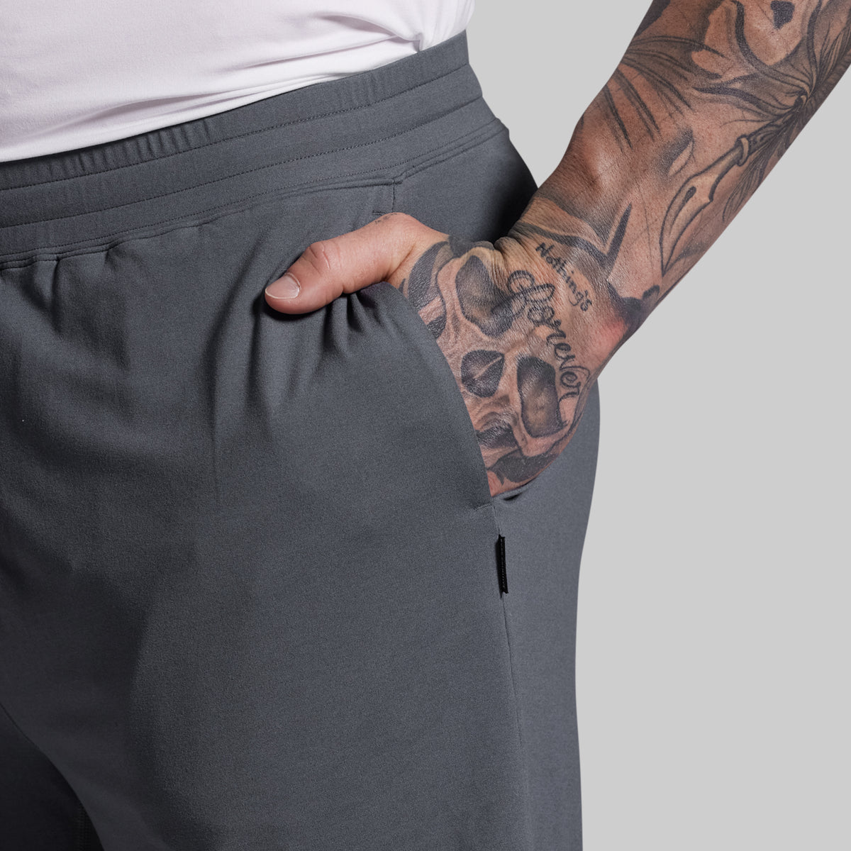 Person wearing gray shorts with a tattooed arm on a light gray background