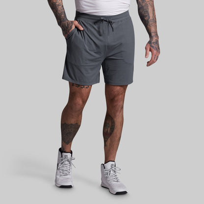 Person wearing gray shorts and white sneakers on a plain background