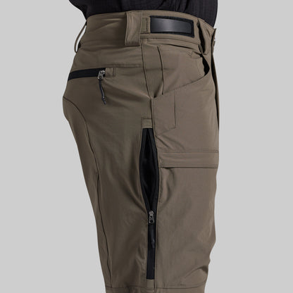 Close-up of a person wearing grey cargo pants with black zipper pockets and a black belt, shown against a light gray background.