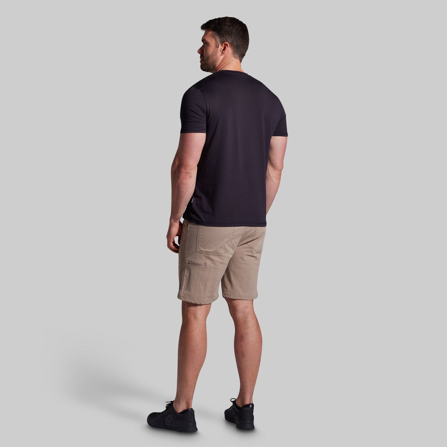 Man wearing a black t-shirt and beige shorts on a light gray background