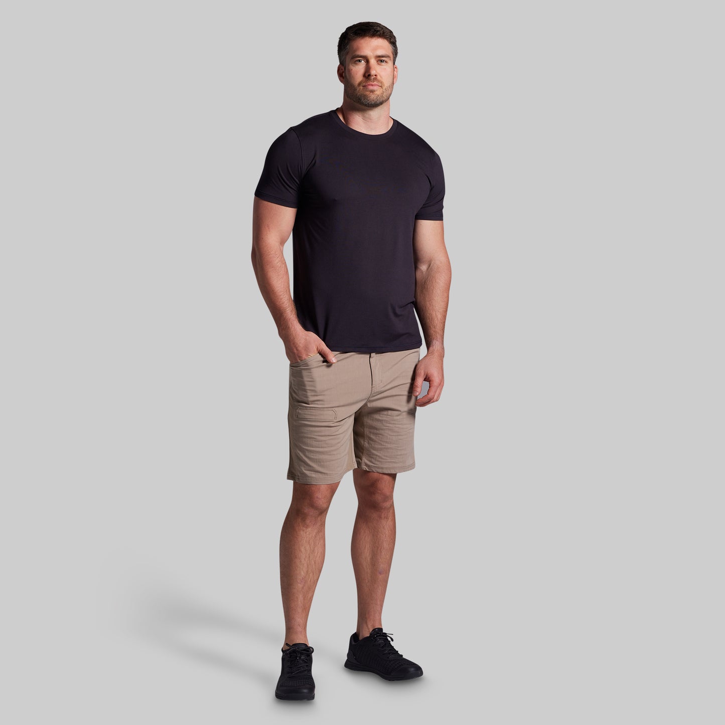 Man wearing a black t-shirt and beige shorts on a gray background