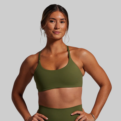 Woman wearing an olive green sports bra and leggings on a gray background