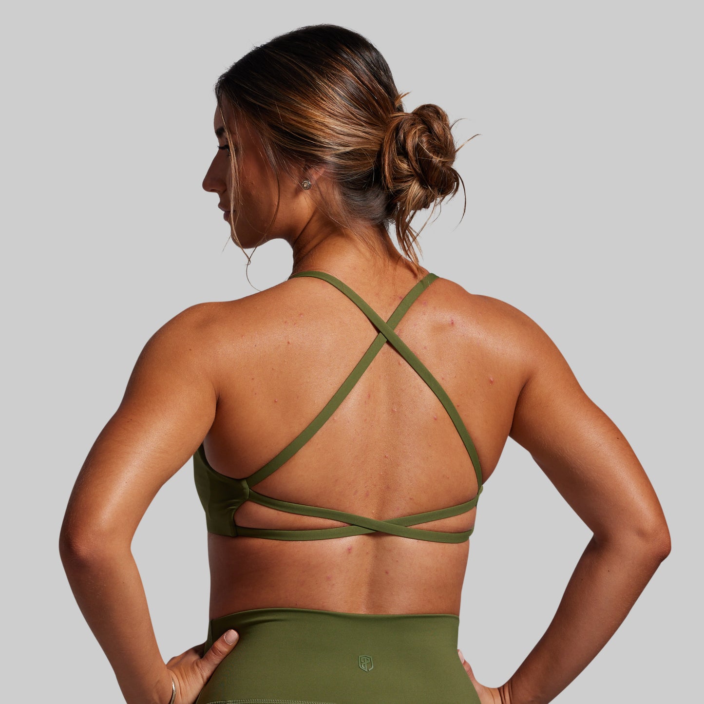 Woman wearing a green sports bra and leggings on a gray background
