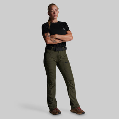 A woman modeling a pair of olive green outdoor cargo pants with a black t-shirt and brown hiking boots, standing against a solid gray background.
