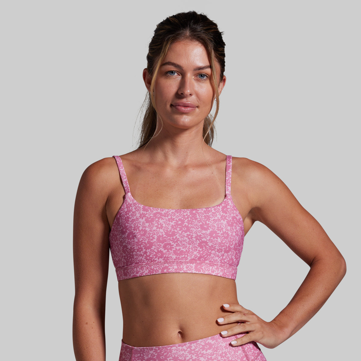 Woman wearing a pink sports bra and leggings against a gray background