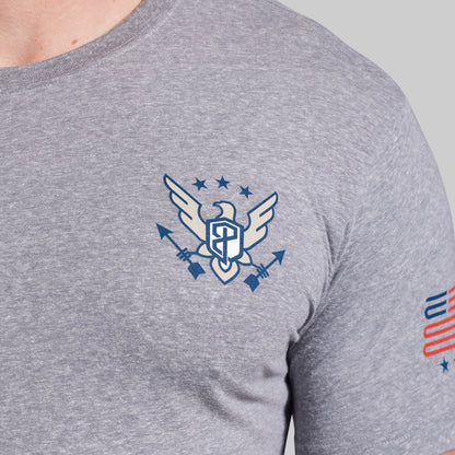 Gray t-shirt with a logo on the chest and American flag design on the sleeve against a gray background