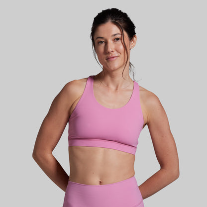 Woman wearing a pink sports bra and leggings on a gray background