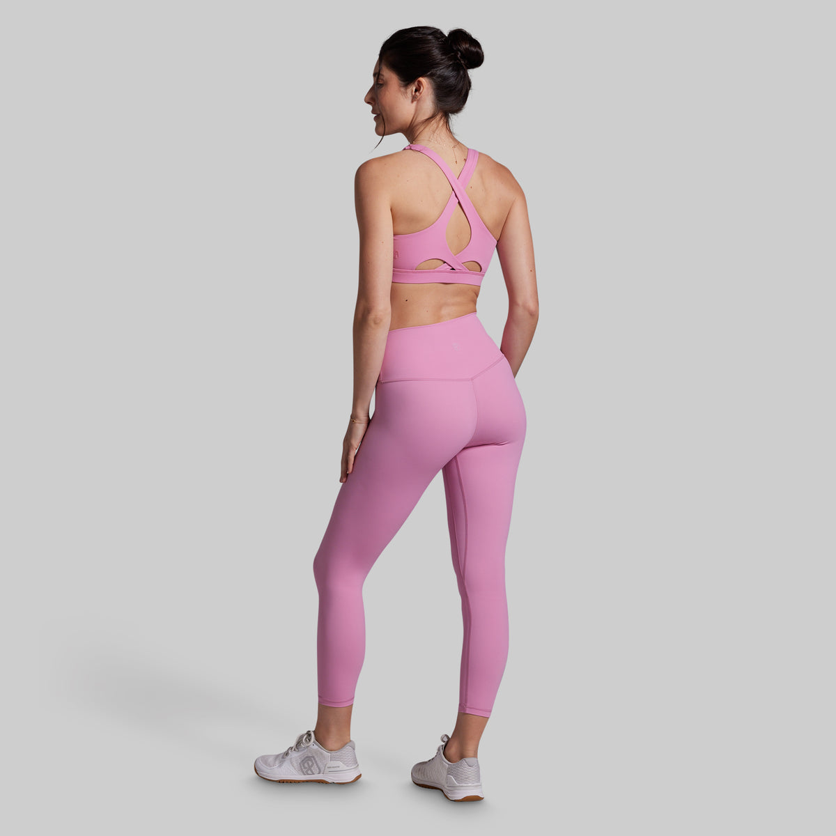 Woman wearing a pink sports bra and leggings set on a gray background