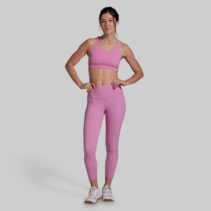 Woman wearing a pink sports bra and leggings set on a gray background