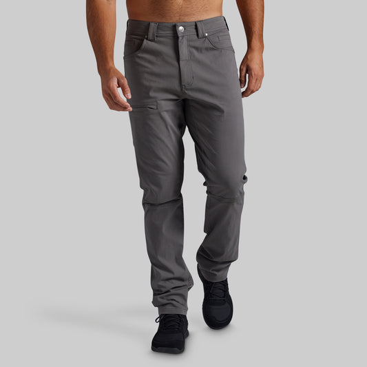 A man wearing dark gray technical cargo pants and black sneakers, shown from the waist down against a solid light gray background.