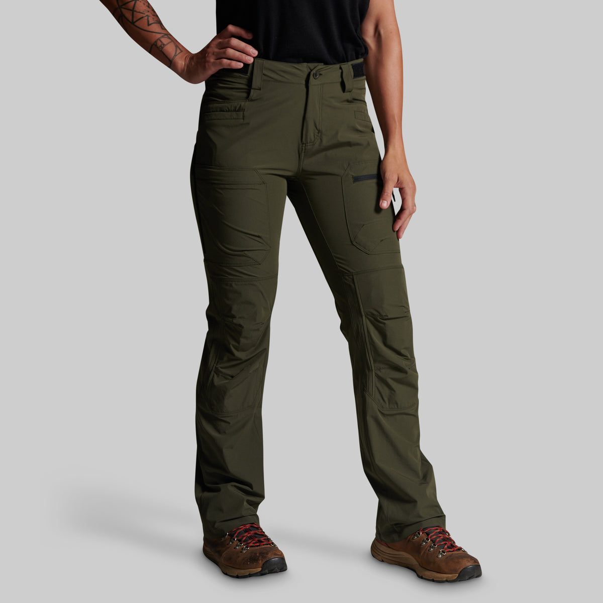 A model wearing olive green technical cargo pants with brown hiking boots, shown from the waist down against a solid gray background.