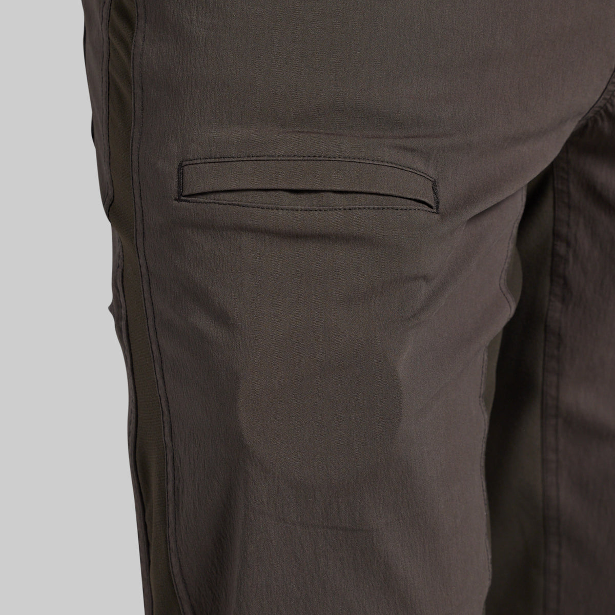 Close-up of dark brown pants showing a side pocket and fabric texture against a light gray background.