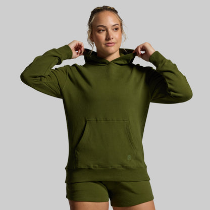 Woman wearing an olive green hoodie and shorts on a gray background