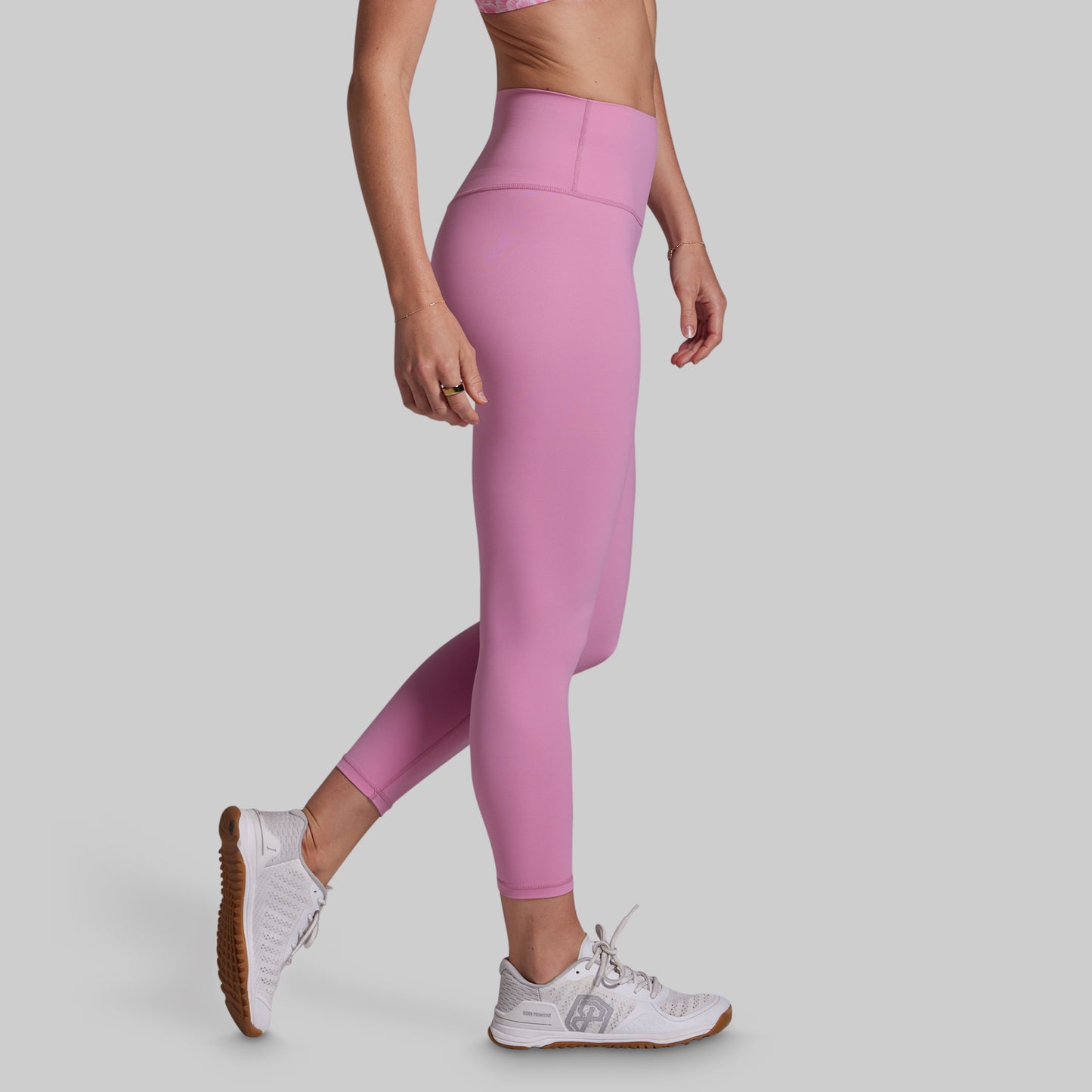 Person wearing pink leggings and white sneakers on a plain background