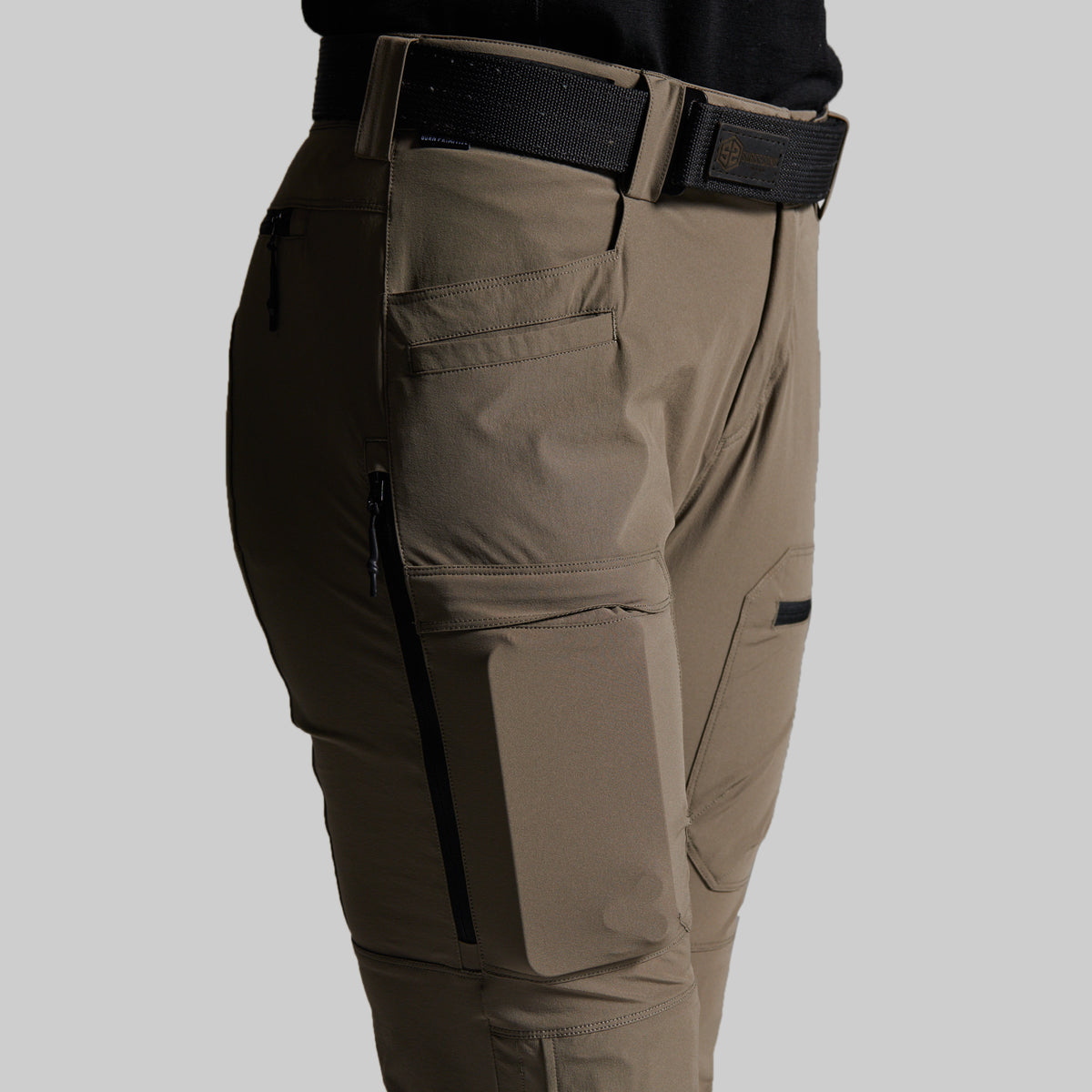 Close-up side view of storm grey cargo pants worn with a black belt, showing side pockets, zippered cargo pockets, and a black waistband on a light gray background.