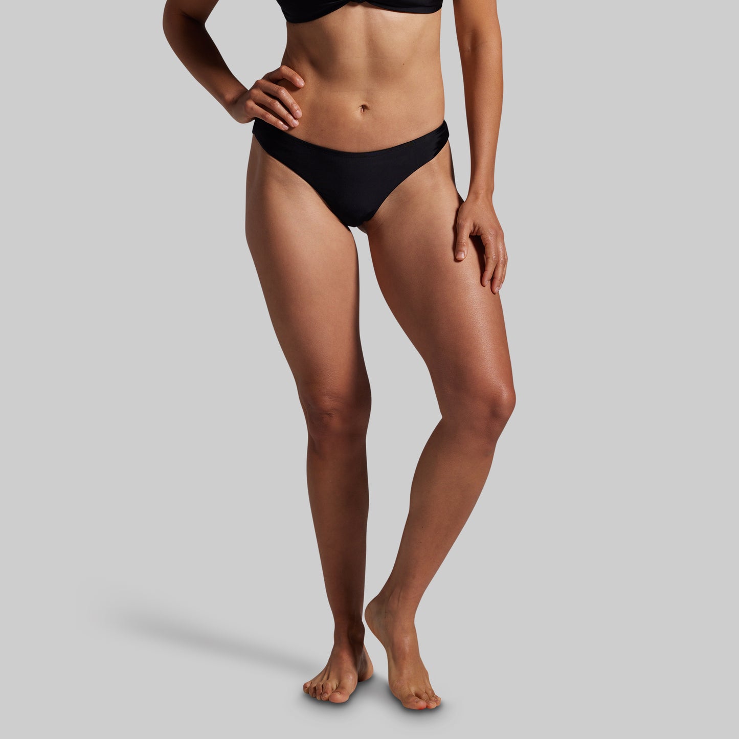 Person wearing black bikini bottoms on a gray background