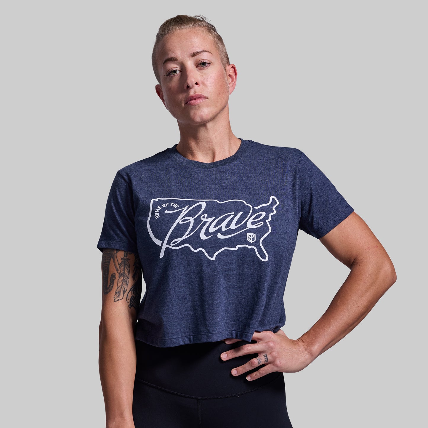 Person wearing a blue t-shirt with 'Home of the Brave' logo on a gray background