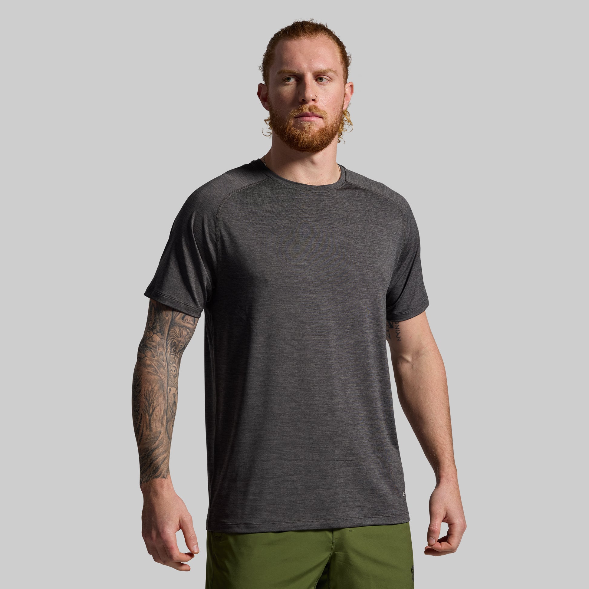 Man wearing a dark gray t-shirt and green pants against a plain background