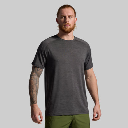 Man wearing a dark gray t-shirt and green pants against a plain background