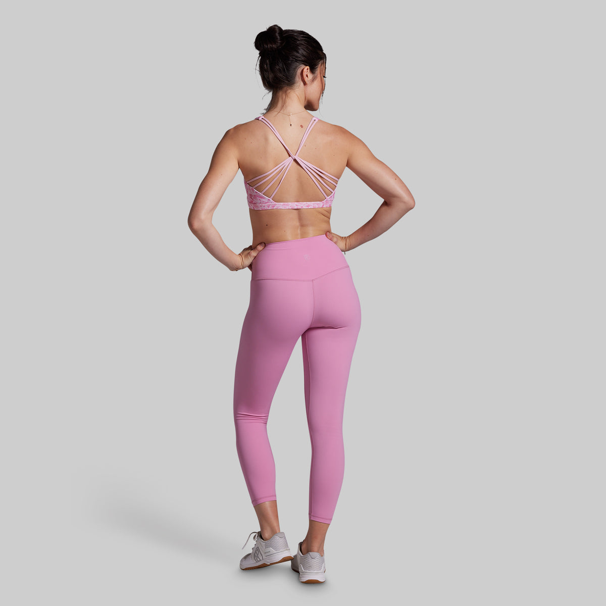 Woman wearing a pink sports bra and leggings set on a light gray background