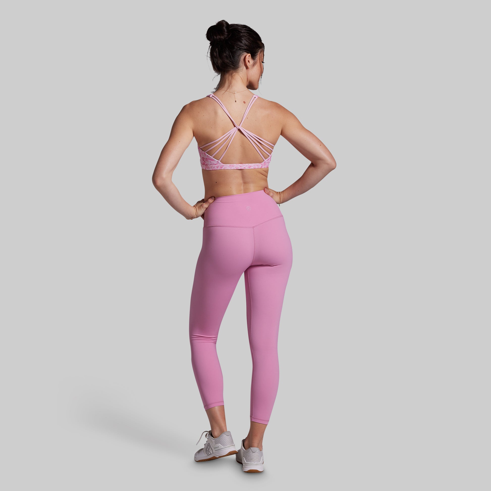 Woman wearing a pink sports bra and leggings set on a light gray background