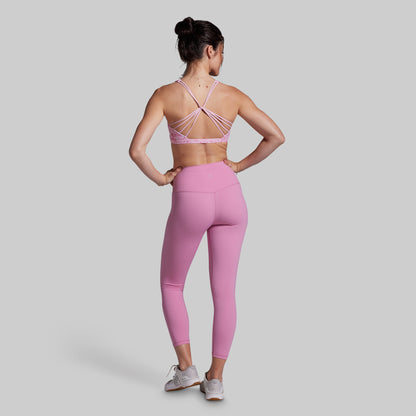 Woman wearing a pink sports bra and leggings set on a light gray background