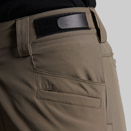 Close-up of a person wearing storm grey outdoor pants with a black belt and a black waistband patch, shown against a light gray background.