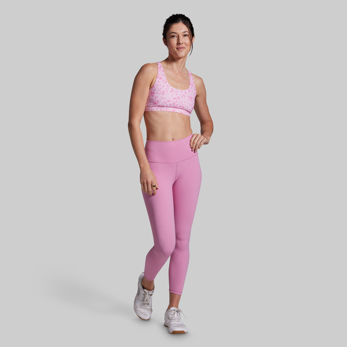 Woman wearing a pink sports bra and leggings on a light gray background