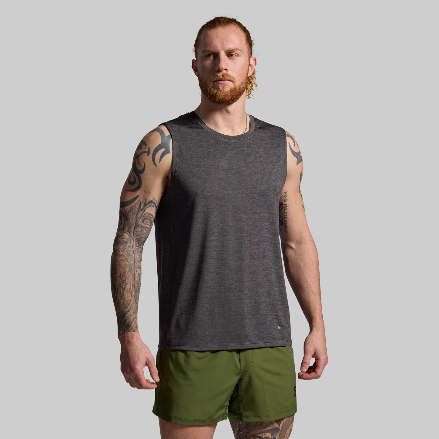 Man wearing a gray sleeveless shirt and green shorts on a gray background