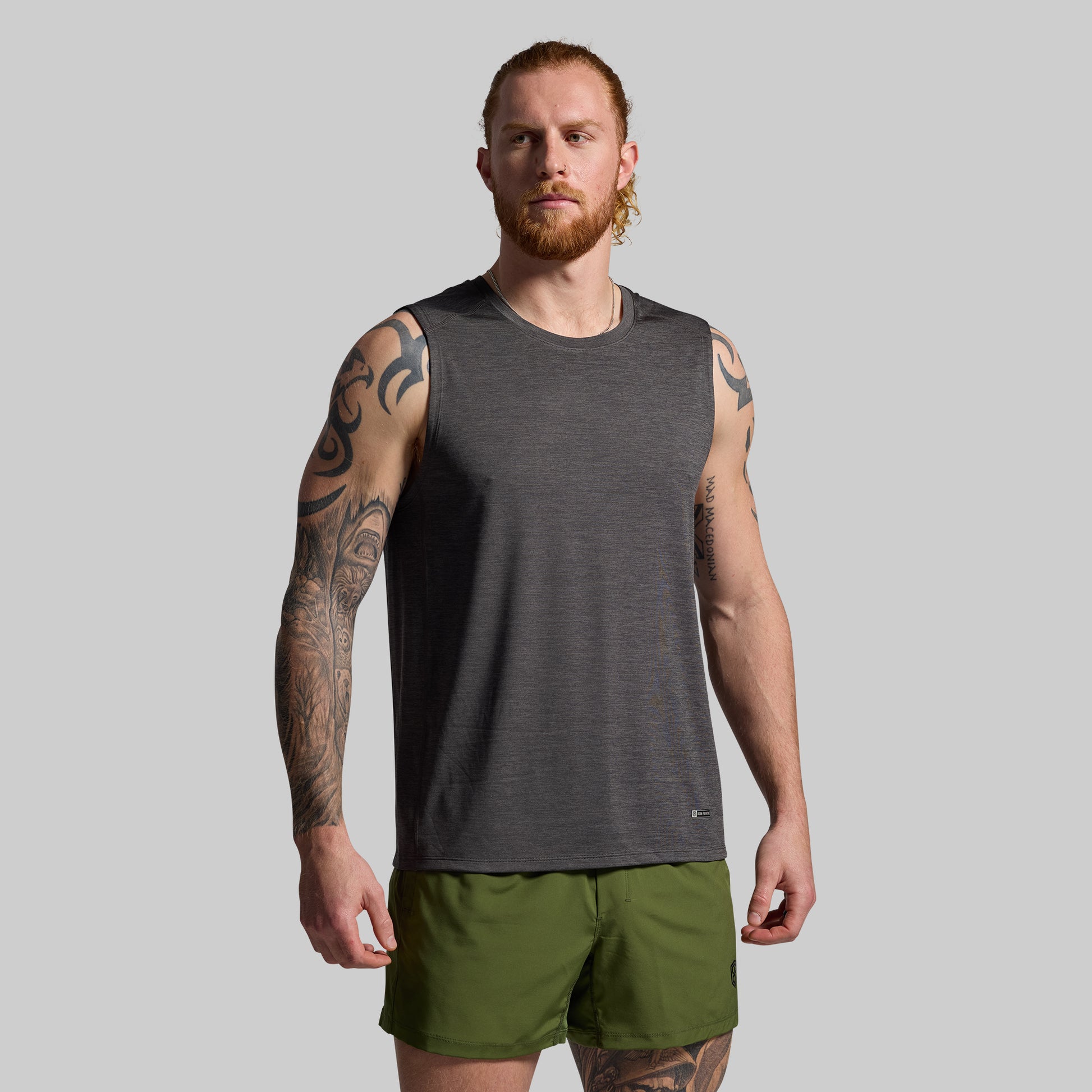 Man wearing a gray sleeveless shirt and green shorts on a gray background