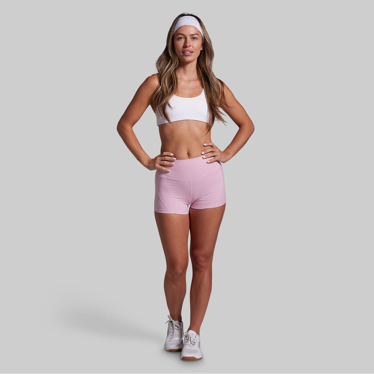 Woman wearing a white sports bra and pink shorts on a gray background