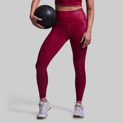 Person wearing maroon leggings holding a black medicine ball on a light gray background