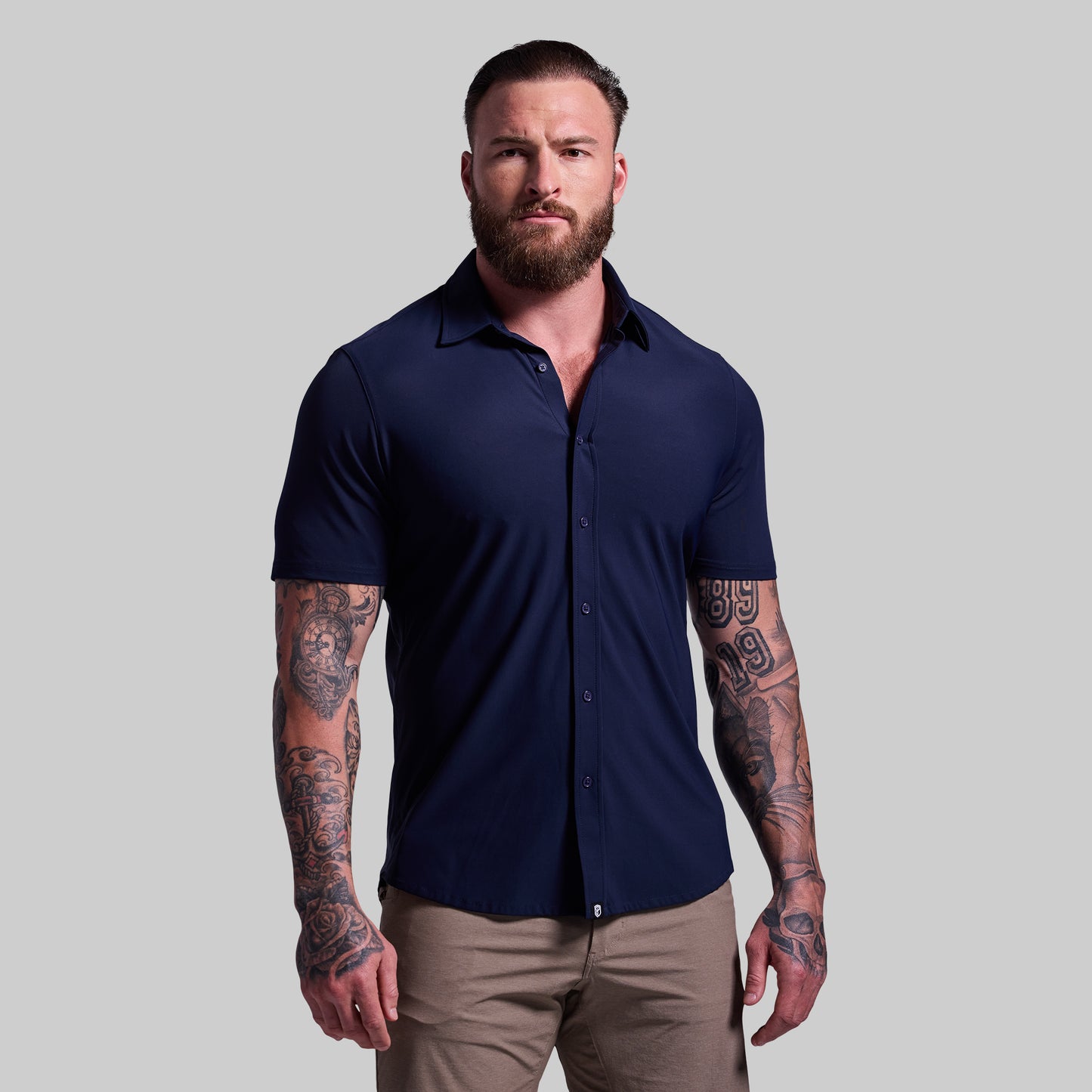 Man wearing a navy blue shirt and beige pants against a gray background