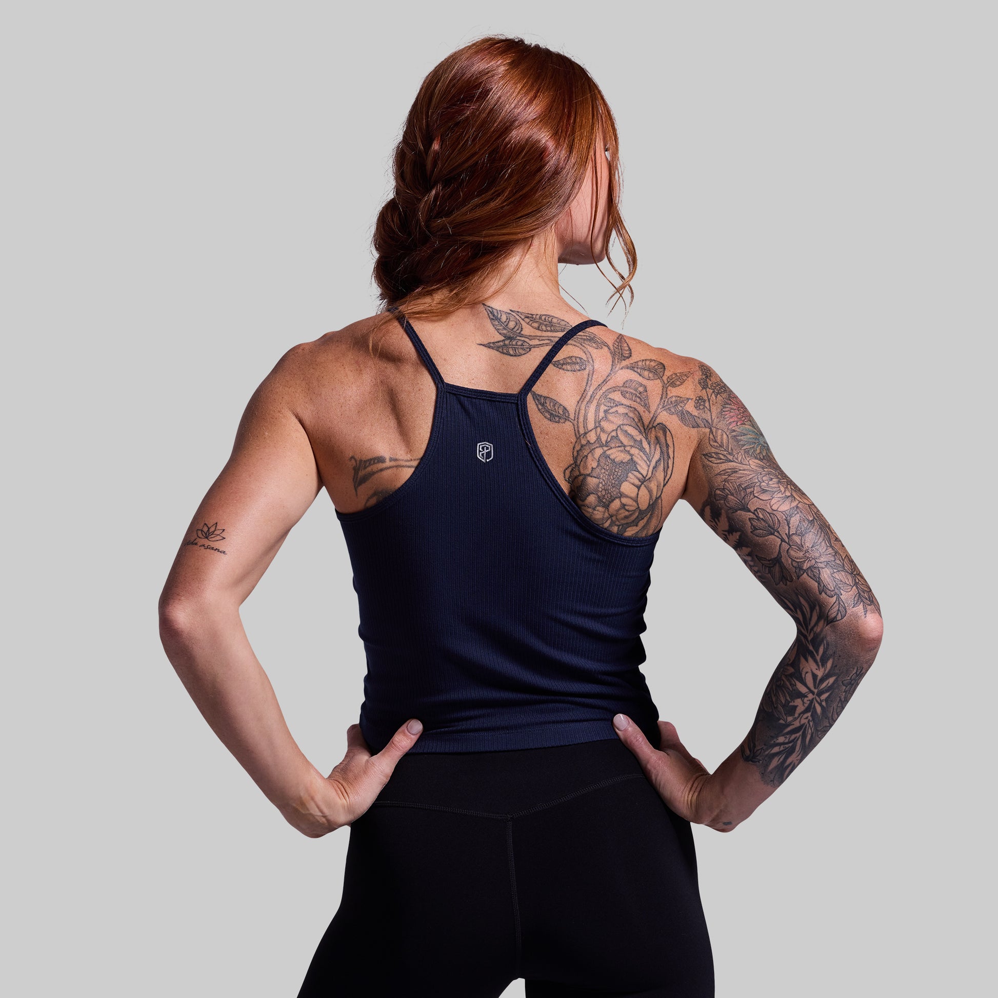 Person wearing a navy tank top with visible tattoos on a plain background