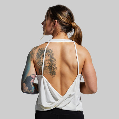 Woman wearing a white strappy top with an open back, showing tattoos on her arms and back.