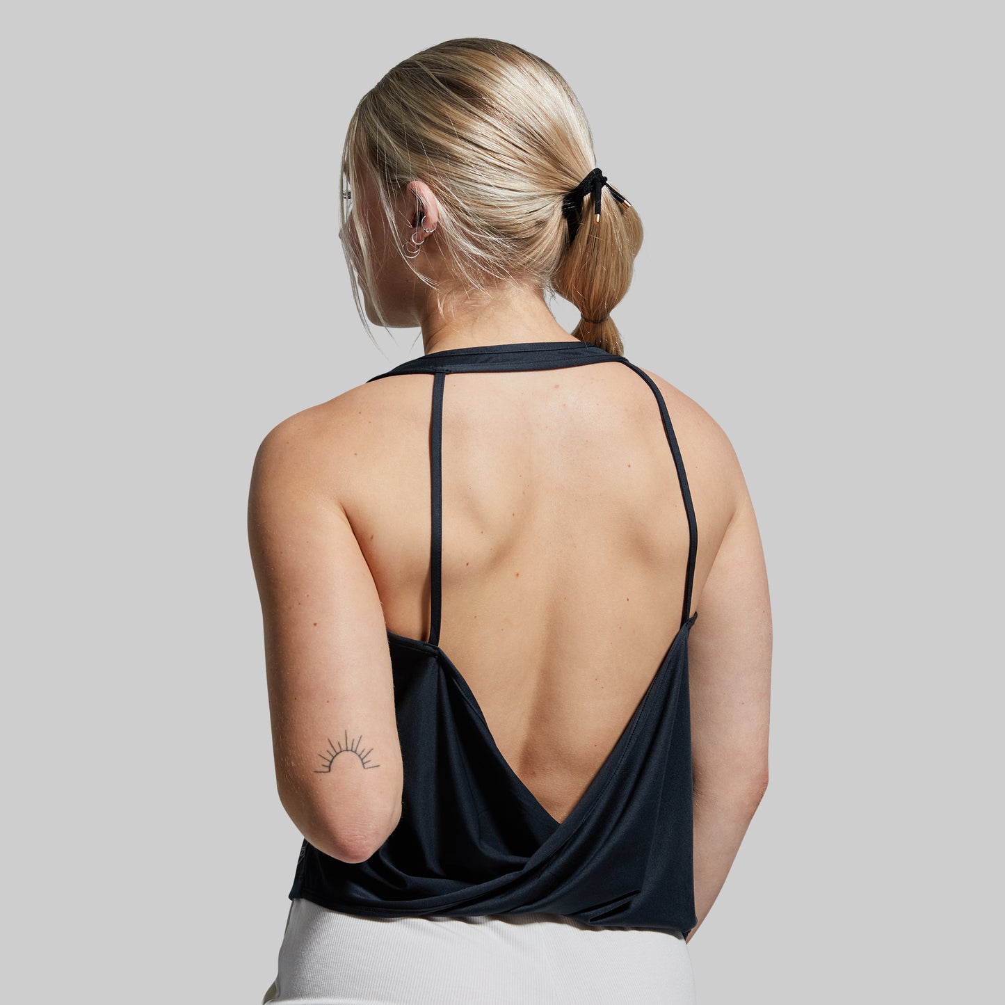 Woman wearing a black strappy top with a plain background