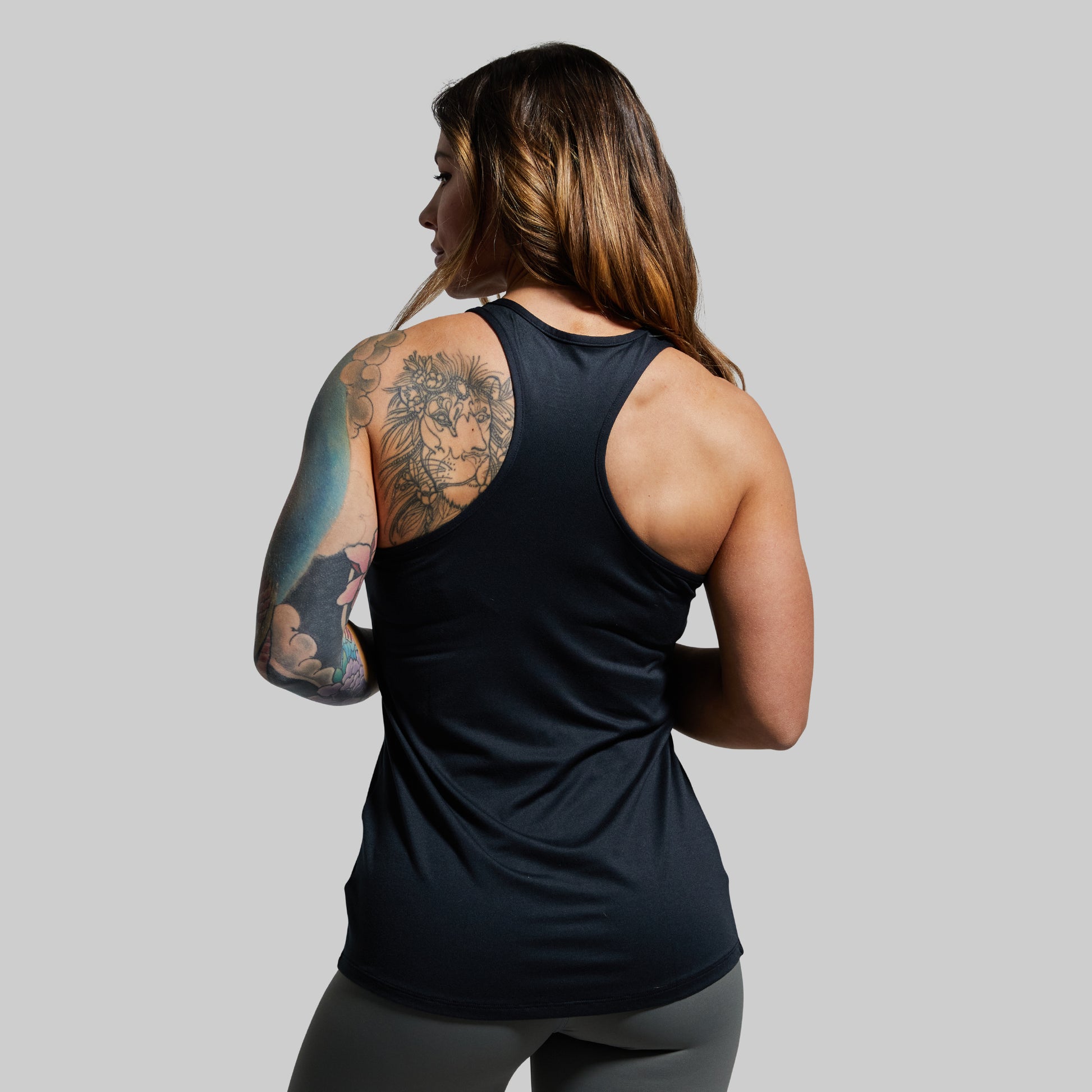Person wearing a black tank top with visible tattoos on a plain background
