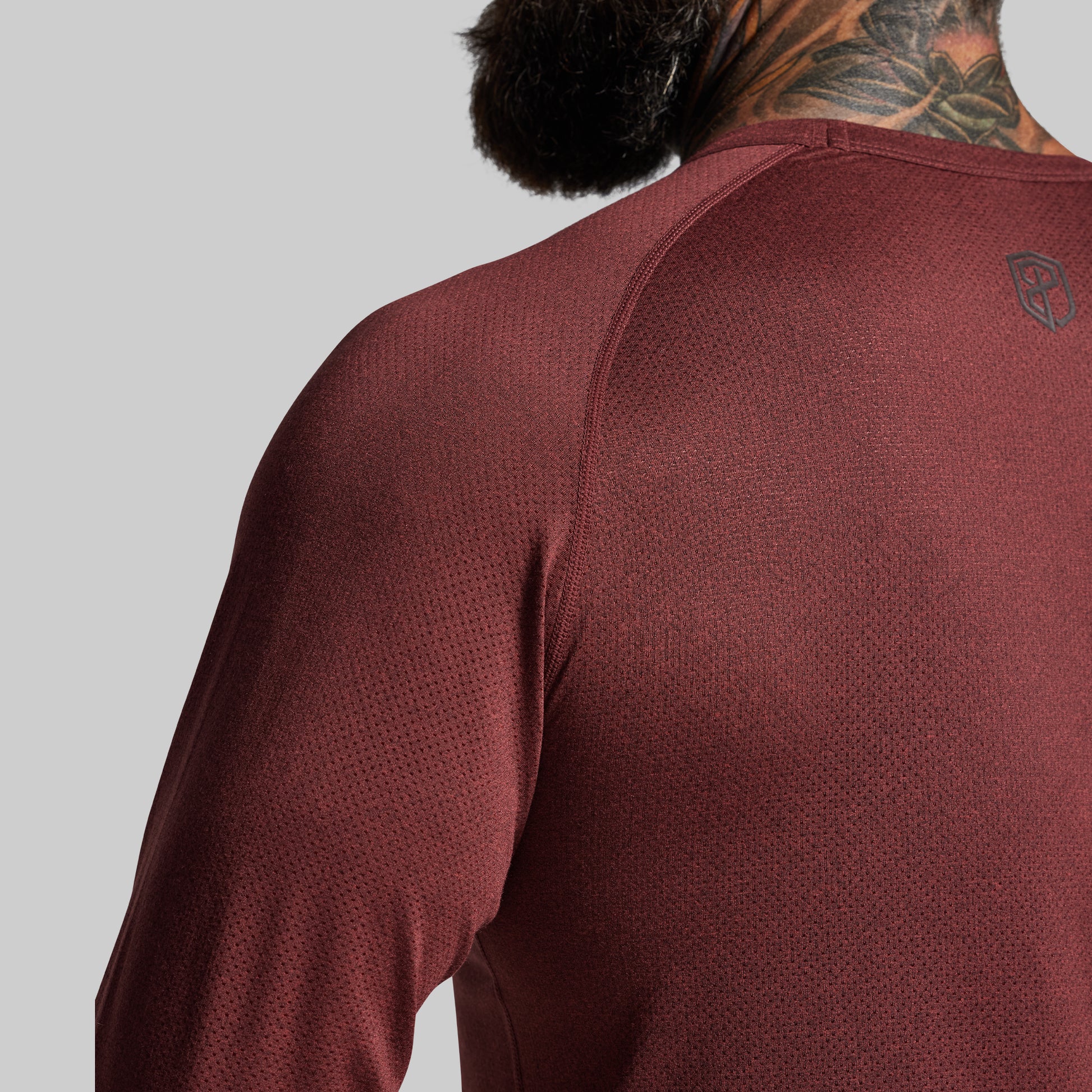 Maroon athletic shirt with a brand logo on the back against a gray background