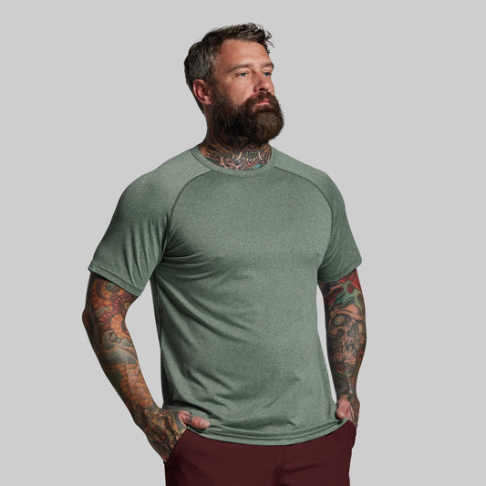 Man wearing a green t-shirt with tattoos on his arms against a gray background