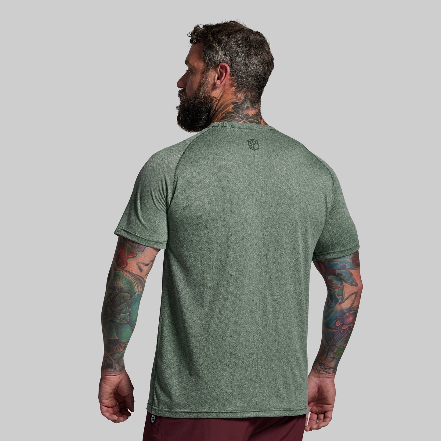 Man wearing a green t-shirt with a small logo on the back against a gray background