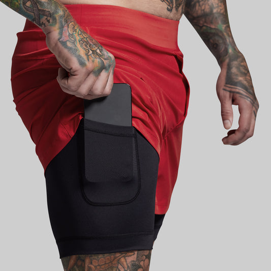Person wearing red shorts with black compression liner with a pocket, on a plain background
