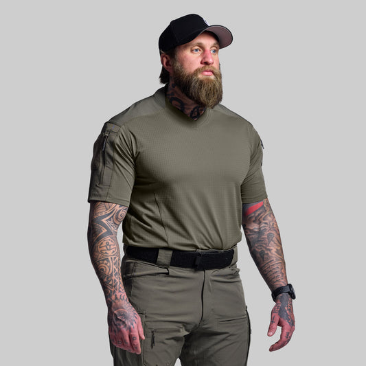 Man wearing a green tactical outfit with tattoos on arms against a gray background