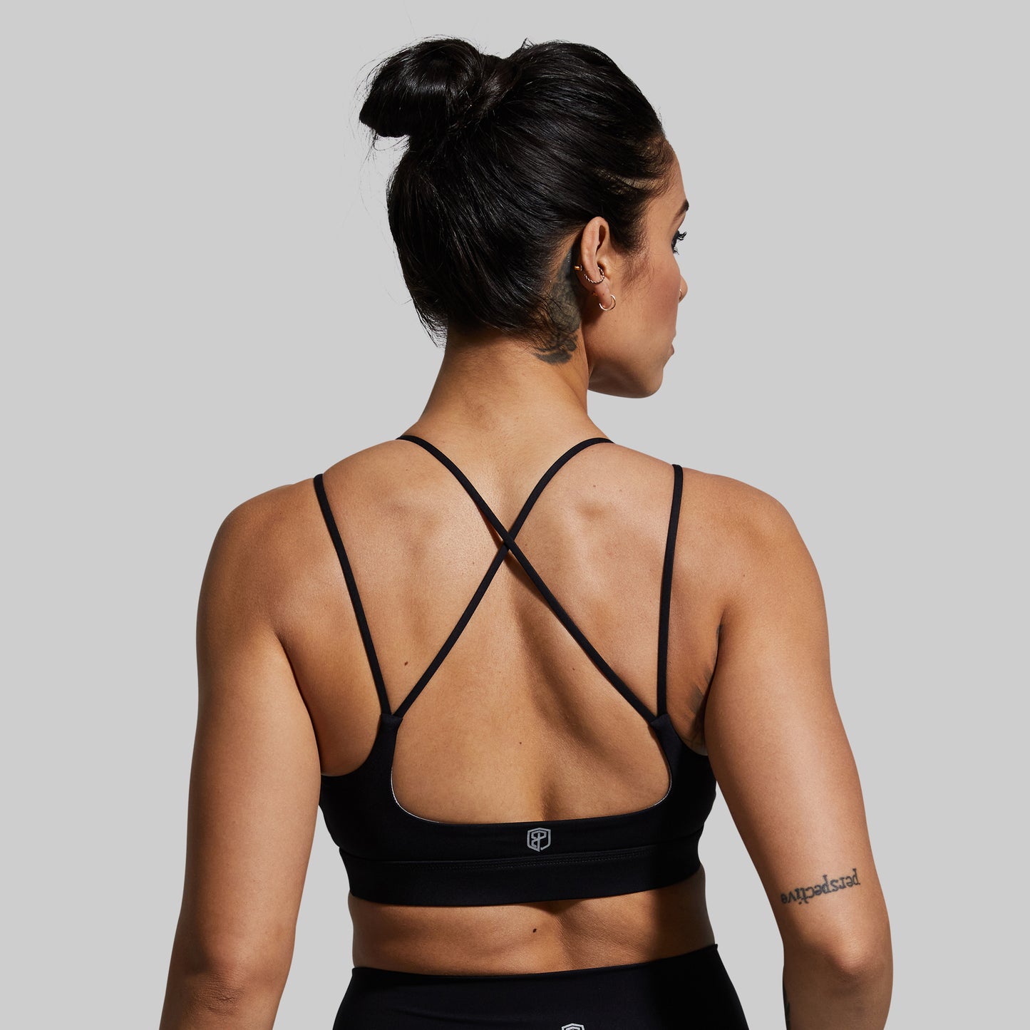 Woman wearing a black sports bra with criss-cross straps on a gray background