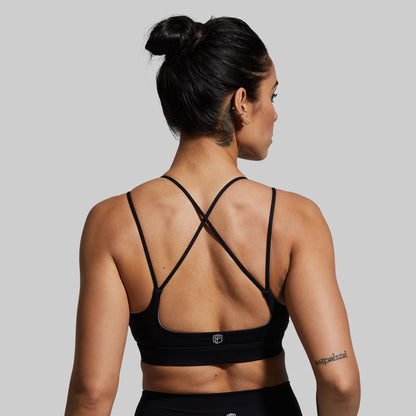 Woman wearing a black sports bra with criss-cross straps on a gray background