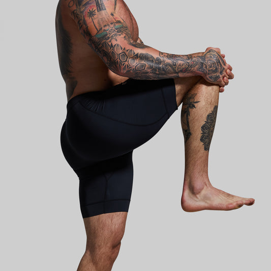 Person wearing black athletic shorts with tattooed legs on a plain background